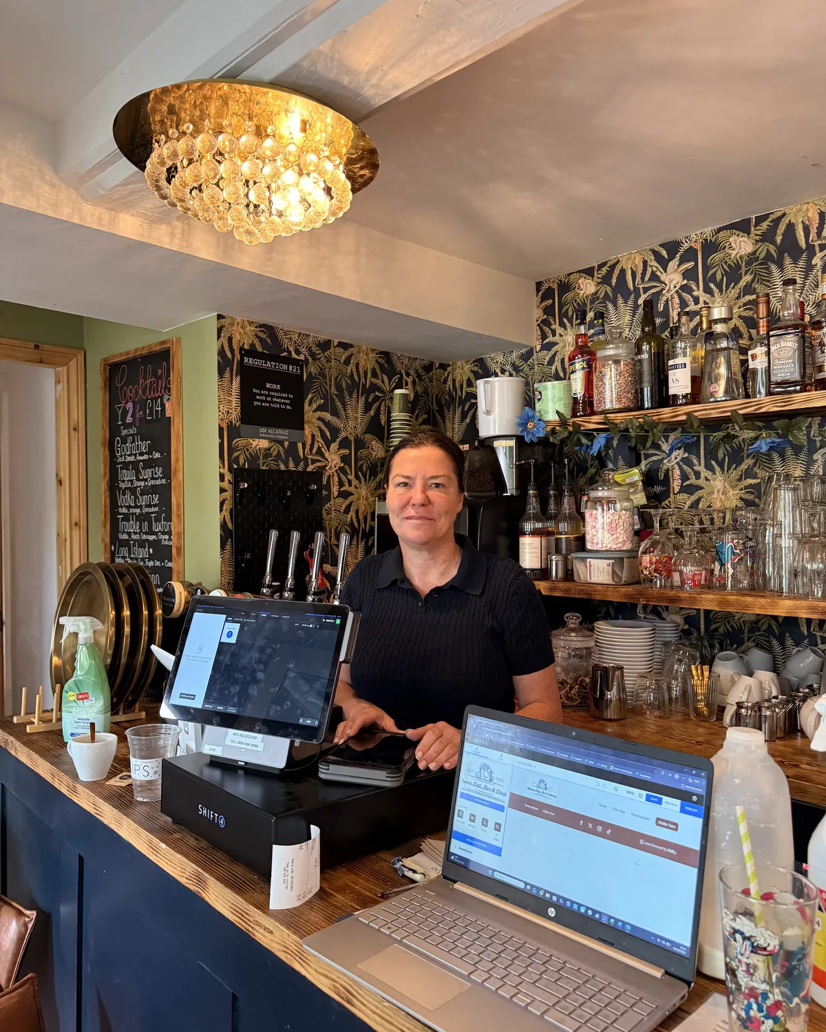 Pub manager taking online payments on a laptop alongside an EPOS till
