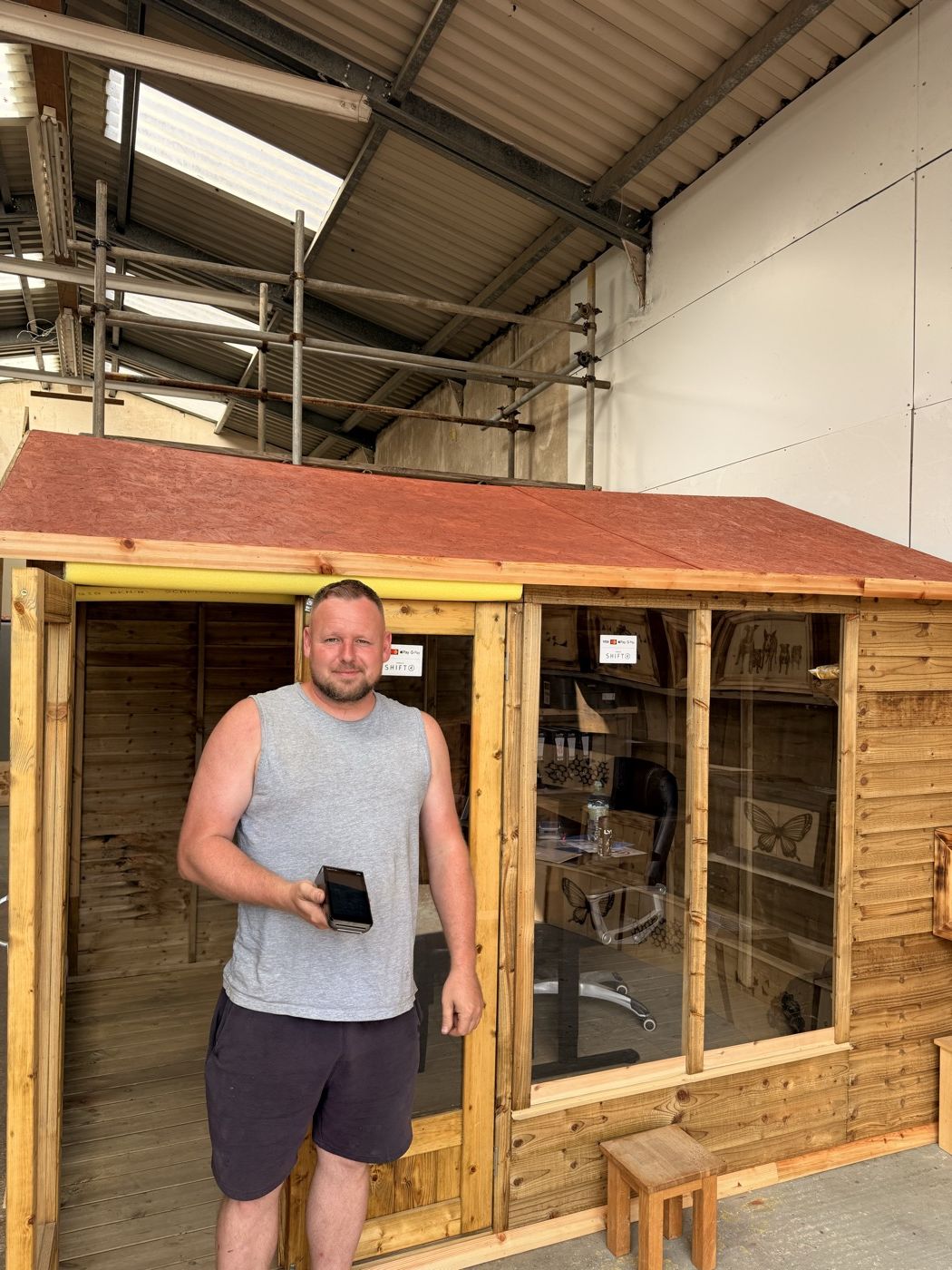 A garden buildings maker holding a card terminal beside a display summerhouse