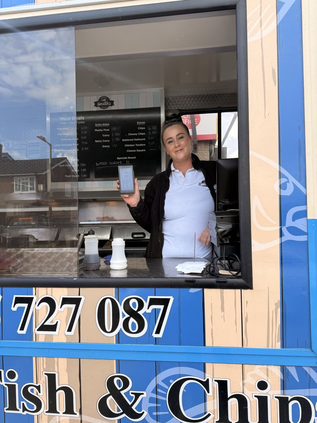 Staff at the serving hatch of Smith's Fish and Chips van holding a card terminal